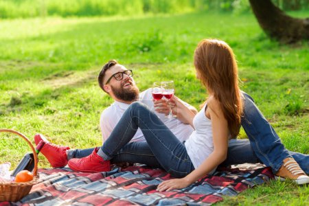 Photo for Couple in love sitting on a picnic blanket in a park holding glasses of wine and making a toast - Royalty Free Image