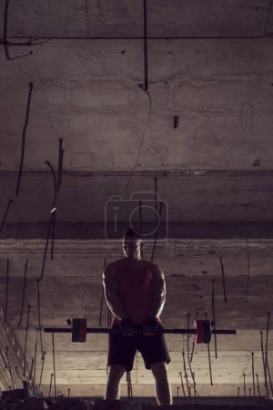 Photo for Young muscular built athlete working out with a barbell, lifting weights in an abandoned building - Royalty Free Image