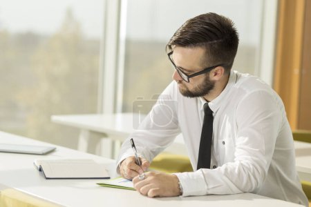 Téléchargez les photos : Homme d'affaires prospère assis dans un bureau et écrivant quelques notes dans son planificateur - en image libre de droit