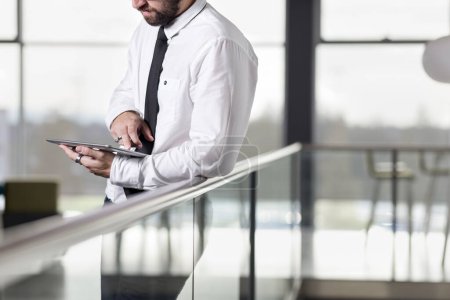 Téléchargez les photos : Homme d'affaires prospère debout dans un immeuble de bureaux, tenant une tablette, se préparant à une réunion - en image libre de droit