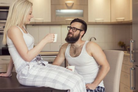 Photo for Young couple in love sitting at the table in the kitchen, drinking morning coffee and chatting. Focus on the guy - Royalty Free Image