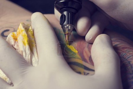 Photo for Male tattoo artist showing the process of making a tattoo on arm. Colorful tattoo art on human body and skin. Tattooist holding an active machine or gun. - Royalty Free Image