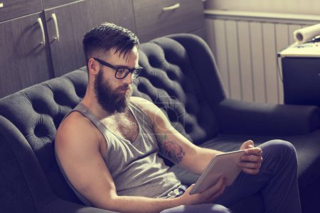 Foto de Modelo masculino sentado en un sofá en una sala de estar, navegar por la web en una tableta - Imagen libre de derechos