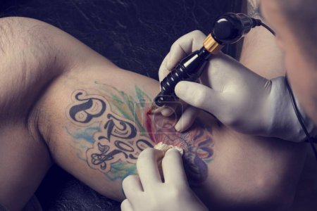 Photo for Male tattoo artist showing the process of making a tattoo on arm. Colorful tattoo art on human body and skin. Tattooist holding an active machine or gun. - Royalty Free Image