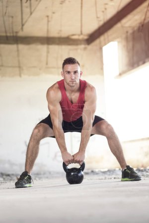 Photo for Young, muscular, athletic built man working out, lifting a kettlebell weight in an abandoned ruined building - Royalty Free Image