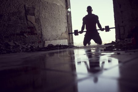 Photo for Muscular, athletic built, young athlete lifting weights in a ruin building next to a puddle of water - Royalty Free Image