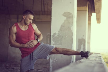 Photo for Muscular, athletic built, young man stretching out in a ruin building before workout - Royalty Free Image