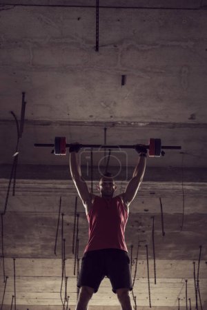 Photo for Young muscular man lifting a barbell in an abandoned building - Royalty Free Image