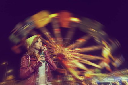 Téléchargez les photos : Belle jeune fille s'amuser et boire du jus au parc à thème - en image libre de droit