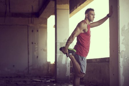 Foto de Musculoso, atlético, joven esparciéndose en un edificio en ruinas antes del entrenamiento - Imagen libre de derechos