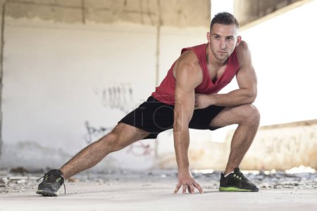 Photo for Muscular, athletic built, young man stretching out in a ruin building before workout - Royalty Free Image