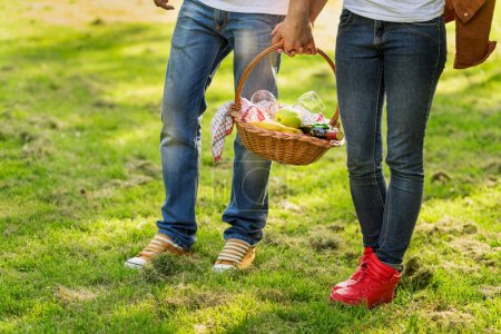 Photo for Couple in love walking through nature, holding hands and carrying a picnic basket - Royalty Free Image