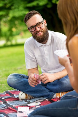 Foto de Pareja enamorada en un picnic en la naturaleza, sentada en un picnic a cuadros, jugando un juego de cartas y divirtiéndose - Imagen libre de derechos