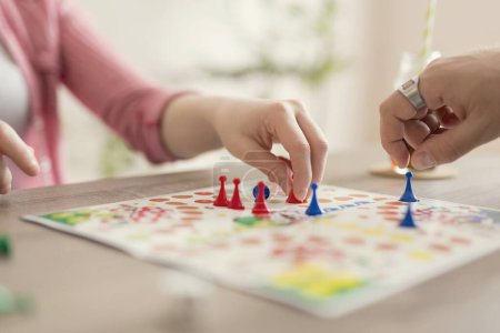Photo for Close up of a couple in love sitting on the floor next to a table, playing ludo board game and enjoying their free time together. Focus on the red figurine - Royalty Free Image