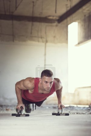 Téléchargez les photos : Musclé, athlétique construit, jeune homme faisant une série de pompes dans un bâtiment en ruine avant l'entraînement - en image libre de droit
