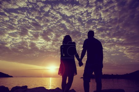 Photo for Silhouette of a couple in love holding hands and looking at a beautiful sunset in Syvota port, Greece - Royalty Free Image