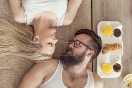 Photo for Top view of a young couple in love lying on a couch, getting up in the morning and having breakfast in bed - Royalty Free Image