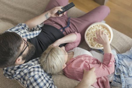Foto de Vista superior de una pareja disfrutando de su tiempo libre, viendo televisión y comiendo palomitas de maíz. Enfoque selectivo - Imagen libre de derechos