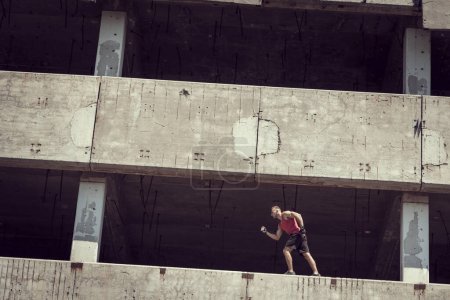 Téléchargez les photos : Jeune homme bâti athlétique faisant du jogging sur les murs minces d'un bâtiment abandonné - en image libre de droit