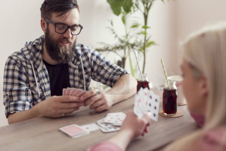 Foto de Pareja joven enamorada sentada en el suelo junto a la mesa, jugando a las cartas, bebiendo jugo y divirtiéndose - Imagen libre de derechos