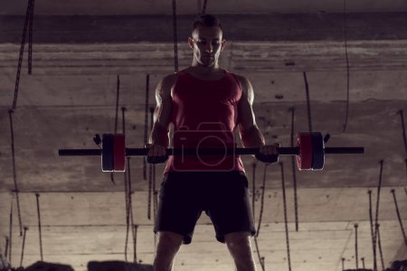 Foto de Joven atleta musculoso construido haciendo ejercicio con una barra, levantando pesas en un edificio abandonado - Imagen libre de derechos