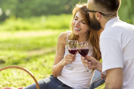 Photo for Couple in love sitting on a picnic blanket in a park holding glasses of wine and making a toast - Royalty Free Image