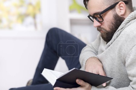 Téléchargez les photos : Homme couché sur le sol, lisant un livre et se relaxant à la maison - en image libre de droit