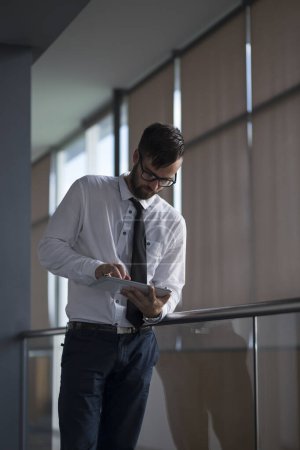 Photo for Successful businessman standing in an office building, holding a tablet computer, preparing for a meeting - Royalty Free Image