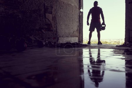 Téléchargez les photos : Musclé, athlétique construit, jeune athlète travaillant dans un bâtiment en ruine à côté d'une flaque d'eau. Entraînement Crossfit avec haltérophilie à cloches et kettlebell - en image libre de droit