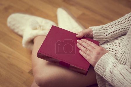 Foto de Detalle de una joven sosteniendo un libro cerrado en su regazo, disfrutando del invierno en un acogedor ambiente hogareño - Imagen libre de derechos