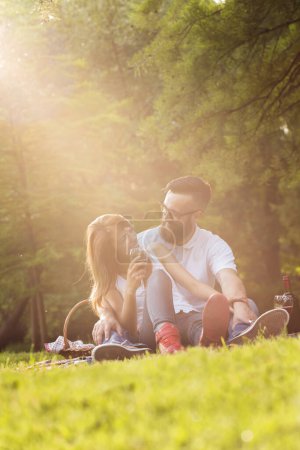 Foto de Pareja enamorada sentada en una manta de picnic en un parque, hablando entre sí, bebiendo vino y disfrutando de un hermoso y tranquilo día en la naturaleza - Imagen libre de derechos