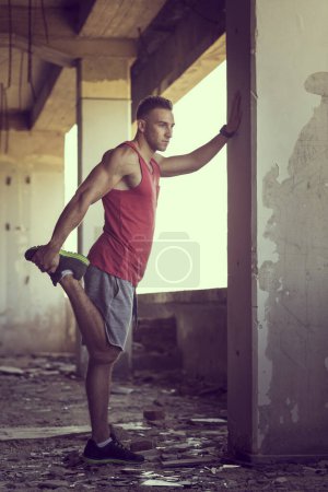 Photo for Muscular, athletic built, young man streching out in a ruin building before workout - Royalty Free Image
