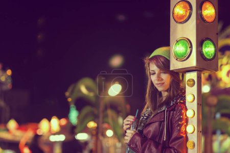 Téléchargez les photos : Belle jeune fille urbaine debout à côté d'un feu de circulation dans un parc d'attractions, boisson énergisante - en image libre de droit