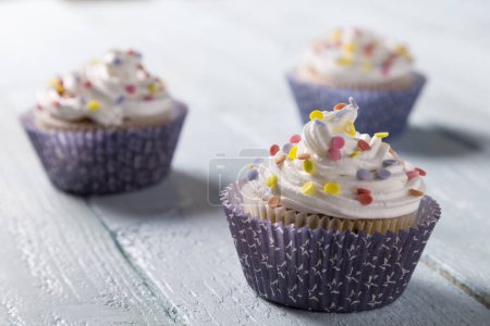 Photo for Three cup cakes with colorful sprinkles on a wooden table - Royalty Free Image