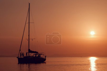 Téléchargez les photos : Silhouette d'un groupe d'amis naviguant sur un voilier avec un beau coucher de soleil en arrière-plan - en image libre de droit