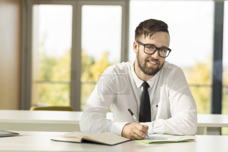 Téléchargez les photos : Homme d'affaires prospère assis dans un bureau et écrivant quelques notes dans son planificateur - en image libre de droit
