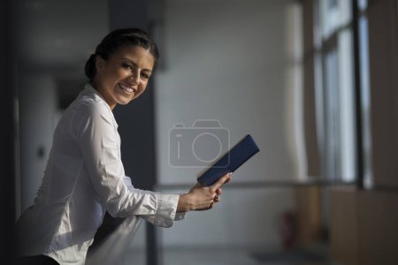 Starke, selbstbewusste Geschäftsfrau, die in einem Bürogebäude steht, einen Notizblock in der Hand hält und sich auf ein Treffen vorbereitet
