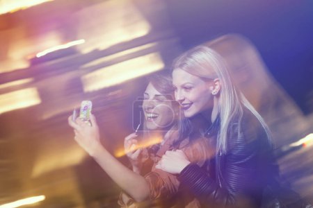 Téléchargez les photos : Deux amies lors d'une soirée entre filles, réparant leur maquillage et s'amusant dans les rues de la ville - en image libre de droit