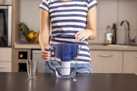 Foto de Detalle de las manos femeninas sosteniendo una jarra de agua filtrada y poniéndole una tapa después de llenarla con un agua del grifo para filtrar - Imagen libre de derechos