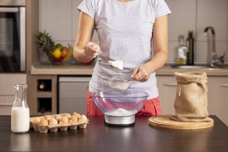 Foto de Detalle de las manos femeninas usando una escala de cocina para medir la harina; mujer midiendo los ingredientes para hacer un pastel, tamizando la harina - Imagen libre de derechos