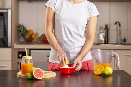 Téléchargez les photos : Détail des mains féminines tenant la moitié du citron et le pressant avec un presse-citron ; femme faisant de la limonade sur un comptoir de cuisine - en image libre de droit