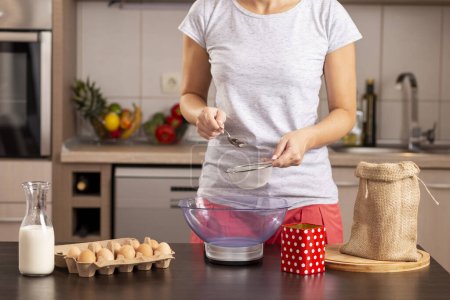 Téléchargez les photos : Détail des mains féminines à l'aide d'une balance de cuisine pour mesurer la farine ; femme mesure les ingrédients pour faire un gâteau, tamiser la farine. Concentrez-vous sur le tamis - en image libre de droit