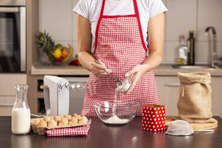 Téléchargez les photos : Détail des mains féminines ajoutant de la farine dans un bol de mélange tout en faisant un gâteau - en image libre de droit