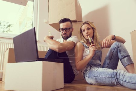 Photo for Young couple in love sitting on the floor of their new appartment, planning redecoration and drinking juice - Royalty Free Image