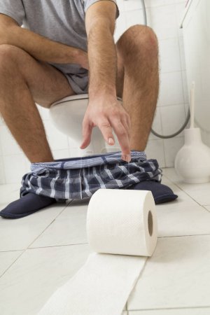 Téléchargez les photos : Détail d'un homme assis sur les toilettes, cherchant du papier toilette. Focus sur la main - en image libre de droit