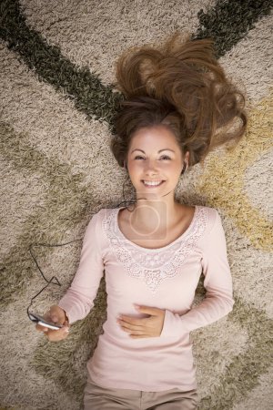 Téléchargez les photos : Vue de dessus d'une belle brune allongée sur le tapis sur le sol de son appartement, écoutant la musique et profitant de son temps libre - en image libre de droit