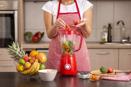 Téléchargez les photos : Détail des mains féminines mettant des tomates fraîches dans un bol de mélangeur pour faire un bouillon de légumes - en image libre de droit