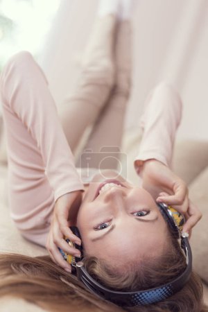 Téléchargez les photos : Jeune femme séduisante allongée sur un canapé dans le salon, portant un casque, écoutant la musique et profitant de sa liberté et de ses loisirs - en image libre de droit