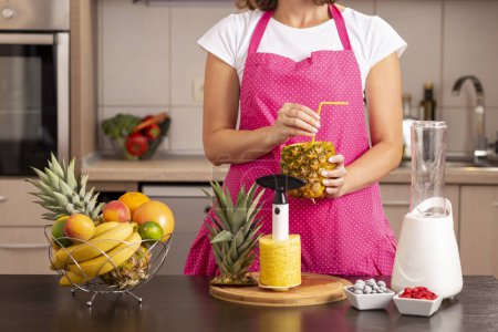 Téléchargez les photos : Femme tenant une peau d'ananas en forme de verre remplie de jus d'ananas frais. Focus sur la main tenant la paille - en image libre de droit