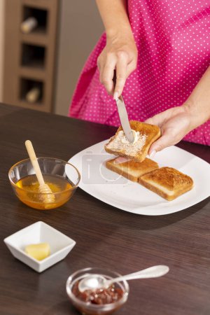 Téléchargez les photos : Détail des mains féminines étaler le beurre sur une tranche de pain grillé, faire un sandwich pour le petit déjeuner. Focus sur le couteau - en image libre de droit